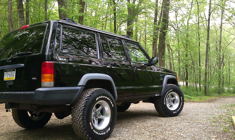 Black 1997 Jeep Cherokee with off-road tires parked on a dirt road in a forest