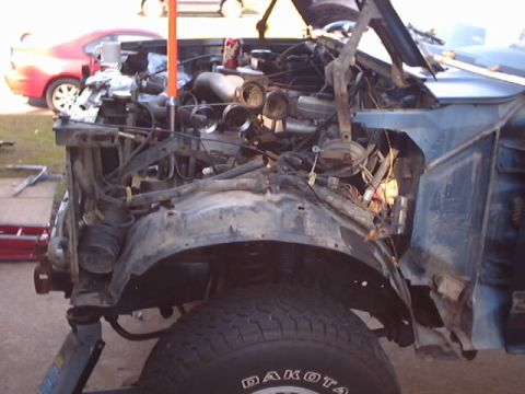 1990 Ford Bronco - The front end of a blue 1990 Ford Bronco shows significant damage and exposed engine parts.