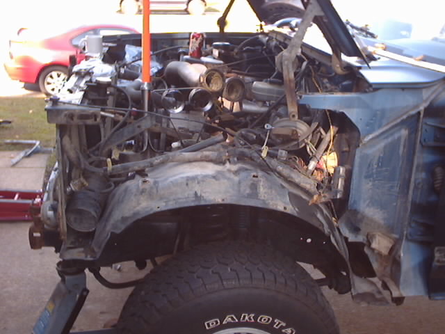 Blue 1990 Ford Bronco front end with damaged bodywork and exposed engine components
