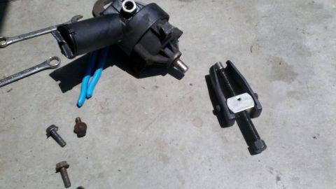 1978 Ford Bronco - A disassembled automotive water pump and a specialized puller tool are laid out on a concrete surface with various bolts and pliers.
