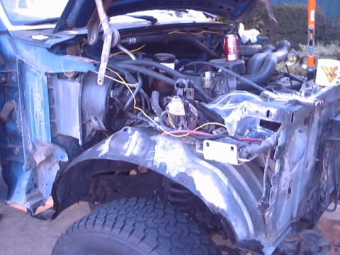 1990 Ford Bronco - The engine bay and front fender area of a blue vehicle are visible, showing extensive body work and exposed mechanical components.
