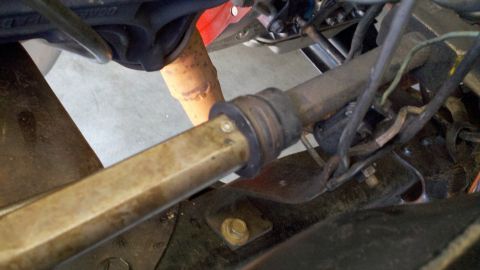 1978 Ford Bronco - This image shows a close-up view of a vehicle's steering column and a rusty exhaust pipe, with some wiring visible.