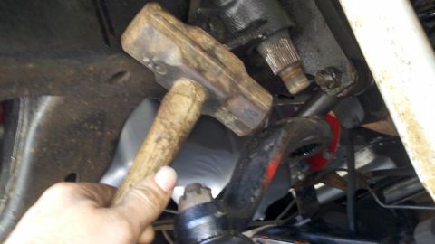 1978 Ford Bronco - A sledgehammer is used to strike the steering linkage of a vehicle, likely for removal or adjustment.