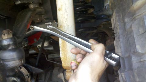 1978 Ford Bronco - Close-up of a hand working on a vehicle's suspension system with an adjustable wrench.