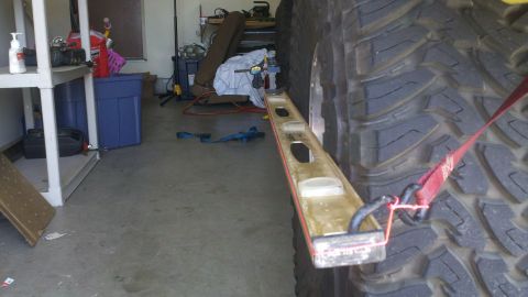 1978 Ford Bronco - A level is used to check the angle of a large tire in a garage setting.