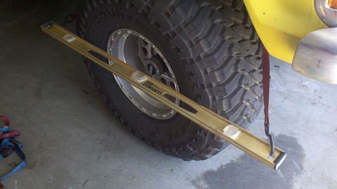 1978 Ford Bronco - A level tool is placed across the tire of a yellow vehicle, with a red strap attached.