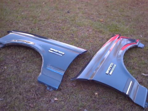 1990 Ford Bronco - Two detached Ford Bronco fenders are shown resting on a grassy surface.