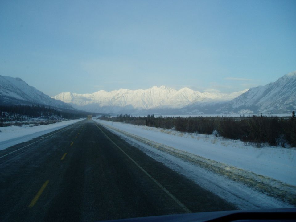 Highway through snowy landscape with mountains under a clear blue sky