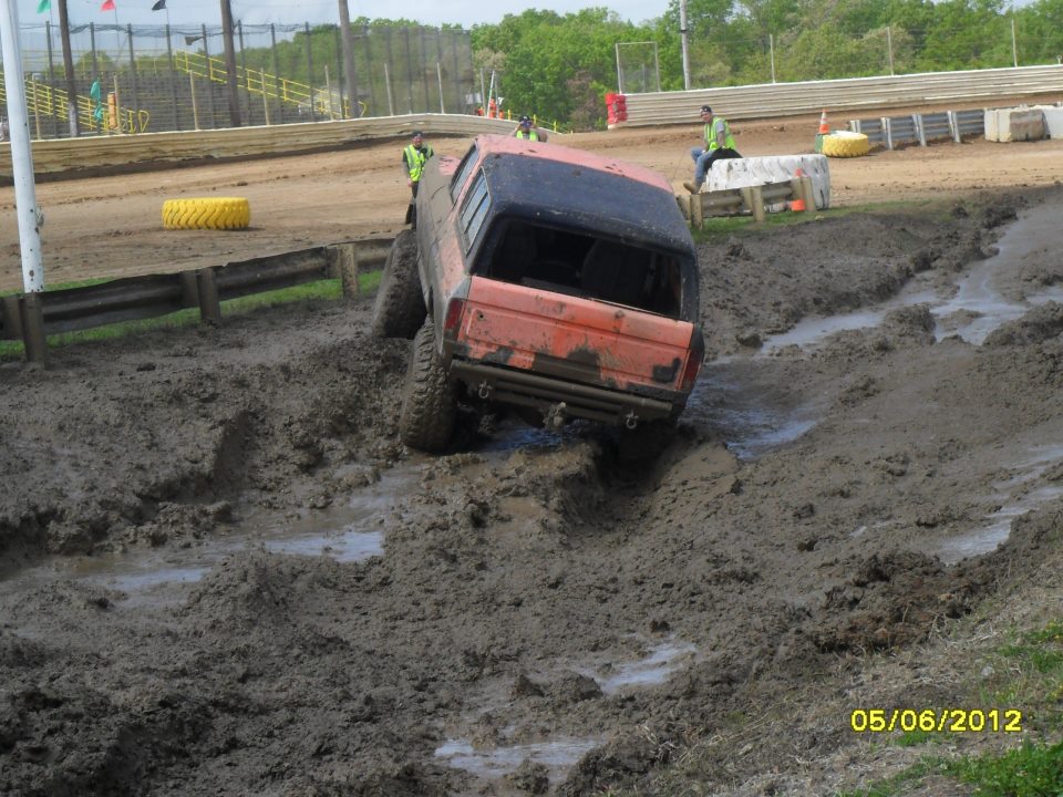 Orange SUV struggling through a muddy track with spectators in the background