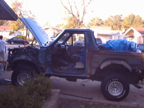 1990 Ford Bronco - A blue pickup truck, likely a 1990 Ford Bronco, is undergoing repairs with its hood open and engine exposed.
