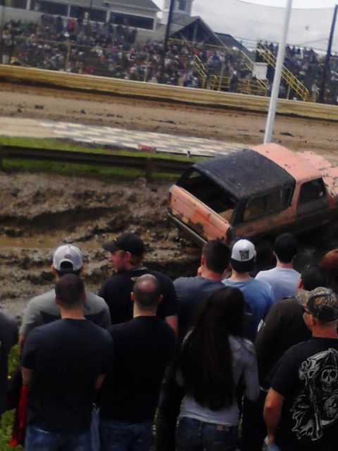 1978 Ford Bronco - An orange SUV is stuck in the mud at a race track, with a crowd of spectators observing.
