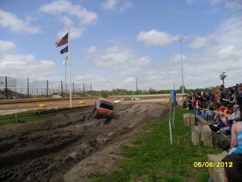 1978 Ford Bronco - A red SUV struggles through a mud pit during an event, with a crowd of spectators observing from the sidelines.