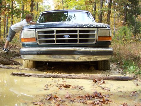 1992 Ford Bronco - A person attempts to push a 1992 Ford Bronco out of a muddy off-road trail.