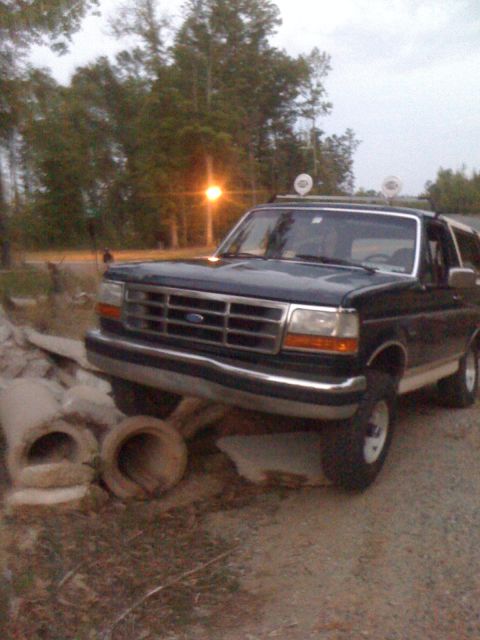 1992 Ford Bronco - A dark blue 1992 Ford Bronco is parked on a dirt road, with large concrete pipes to its left.