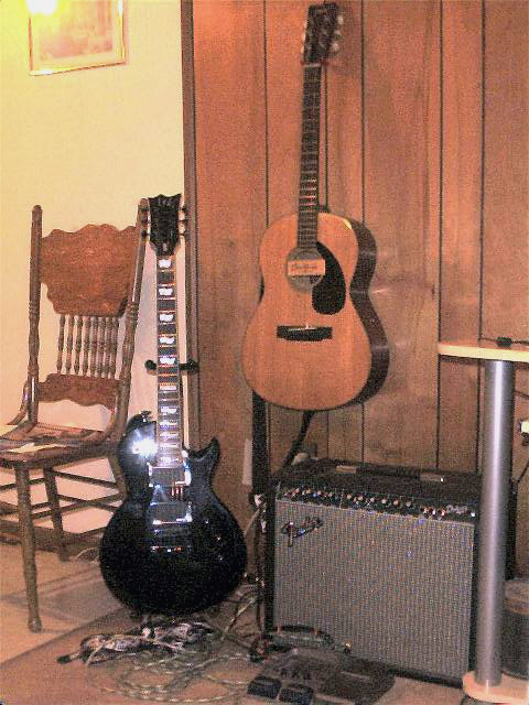 1990 Ford Bronco - Two guitars, an amplifier, and a chair are set up in a room with wood-paneled walls.