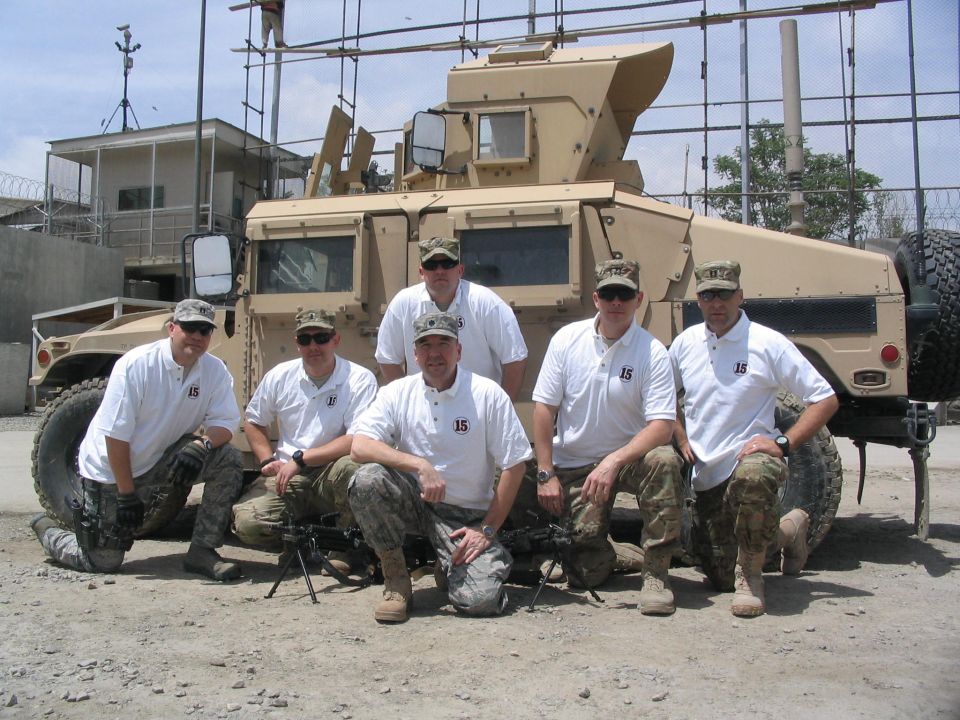 Six soldiers in uniform pose in front of a tan military truck