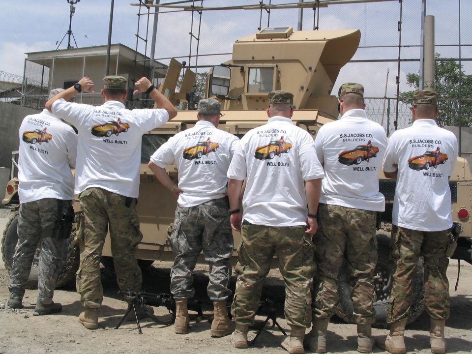 Military vehicle with soldiers wearing shirts showing a classic car graphic