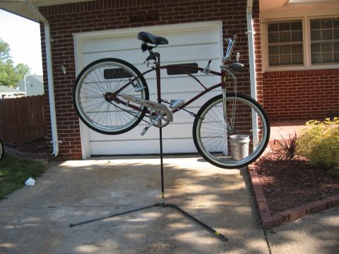 1994 Ford Bronco - A maroon cruiser bicycle is mounted on a repair stand in front of a garage.