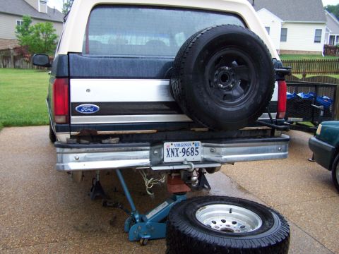 1992 Ford Bronco - The rear of a Ford Bronco is shown lifted by a jack, with a spare tire removed and placed on the ground.