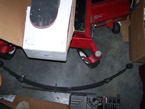 1992 Ford Bronco - A leaf spring and a section of a red lawnmower deck are laid out on a concrete floor.