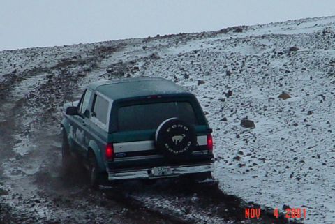 1996 Ford Bronco - A green 1996 Ford Bronco navigates a snowy, rocky incline, kicking up dirt and mud.
