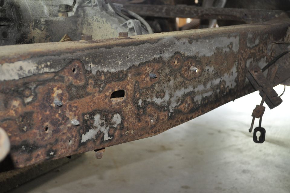 Heavily rusted vehicle frame with visible holes and corrosion