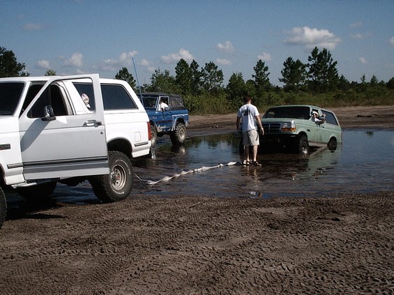 White lifted Ford Bronco pulling a green Bronco out of water with a tow strap