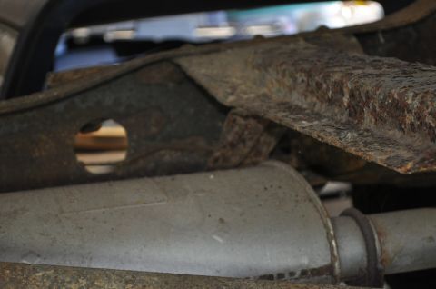 1986 Ford Bronco - The underside of a vehicle shows significant rust on its frame and exhaust system components.