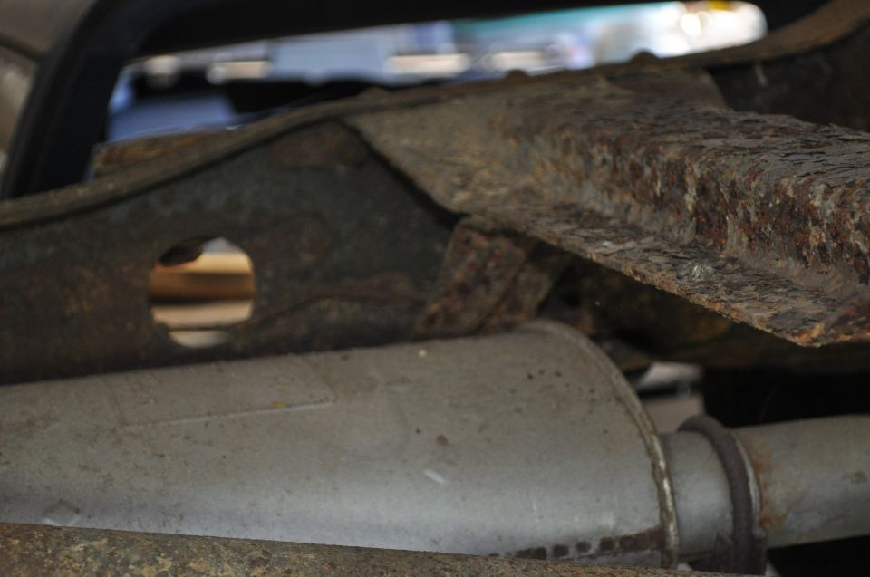 Close-up of heavily rusted vehicle frame and exhaust pipe. Supermotors.net logo visible