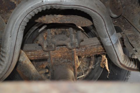 1986 Ford Bronco - Underside view of a heavily rusted rear axle and exhaust system, showing leaf springs and a differential housing.