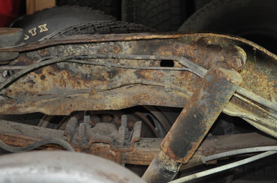 Close-up of heavily rusted frame, leaf springs, and shock absorber from a vehicle's undercarriage