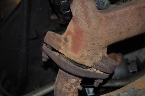 1986 Ford Bronco - Close-up of a corroded exhaust manifold flange, showing a significant crack and fasteners.