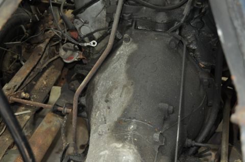 1986 Ford Bronco - Close-up view of greasy engine and transmission components, with visible wiring and metal linkages.