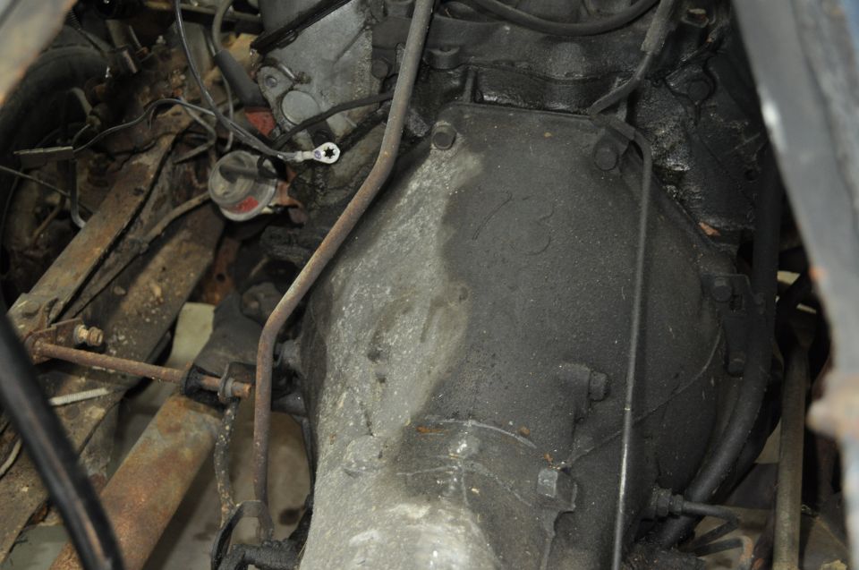Engine and transmission assembly with oil and grime, showing various metal parts and wiring