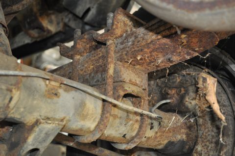 1986 Ford Bronco - Close-up of a heavily corroded rear axle and leaf spring suspension component.