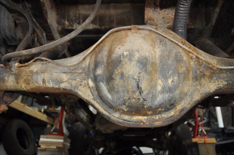 1986 Ford Bronco - The underside of a vehicle's rear differential shows significant rust and wear, with brake lines and suspension parts attached.