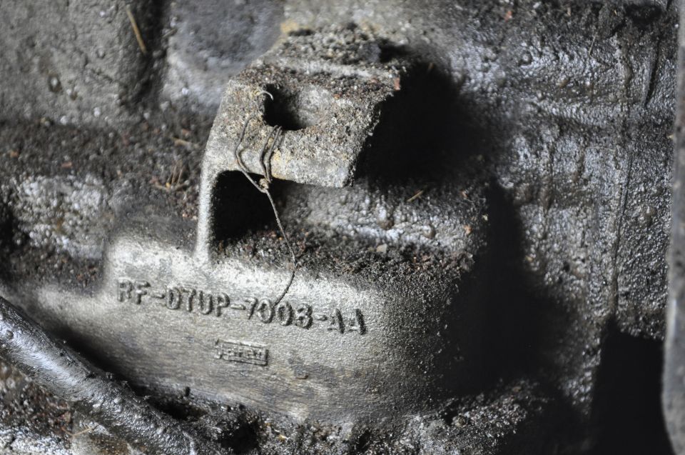 Dirty cast metal part stamped RF-D7UP-7003-AA with wire through a cast loop