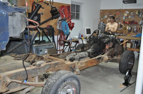 1986 Ford Bronco - A heavily rusted vehicle chassis is being worked on in a garage, with the engine exposed and front cab visible.