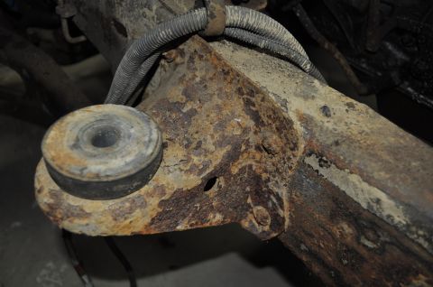 1986 Ford Bronco - Close-up of a heavily rusted vehicle frame component with a rubber bushing and wiring harness.