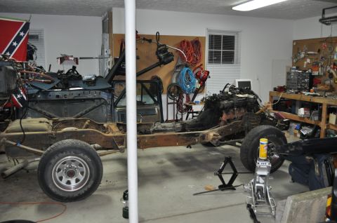 1986 Ford Bronco - A vehicle is disassembled in a garage, with its frame, engine, and various parts laid out for repair or restoration.