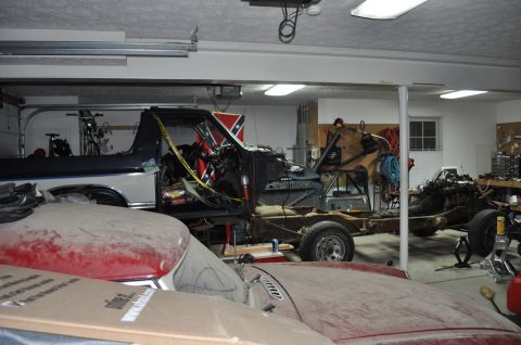 1986 Ford Bronco - A disassembled truck sits in a garage, partially covered by other vehicles and project parts.