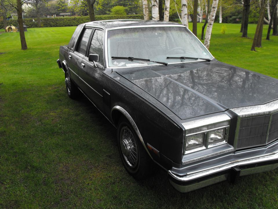 Front quarter view of a dark-colored sedan with chrome trim and wire wheels, parked on a grassy lawn