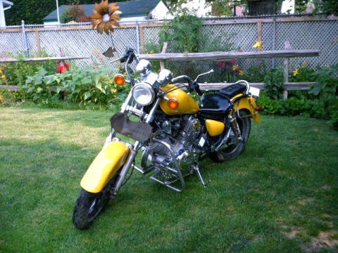 1976 Yamaha Virago - A yellow motorcycle sits on a grassy lawn in front of a wooden fence and garden.
