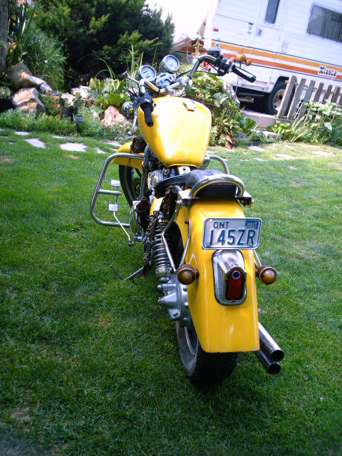 1976 Yamaha Virago - A yellow motorcycle with dual exhaust pipes is shown from the rear, parked on a grassy lawn.
