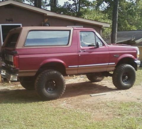 1995 Ford Bronco - A side view of a maroon and tan Ford Bronco with aftermarket wheels and tires, parked outdoors.