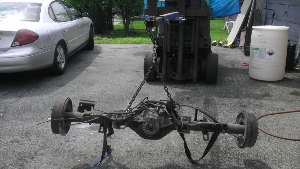 Rear axle assembly with drum brakes, suspended by chains from a forklift