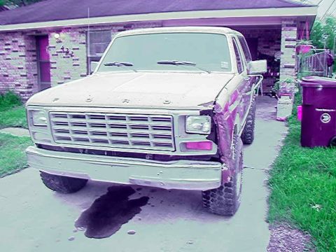 1980 Ford Bronco - Front view of a 1980s Ford truck in primer and bare metal sitting in a residential driveway, missing its passenger-side front fender and he…