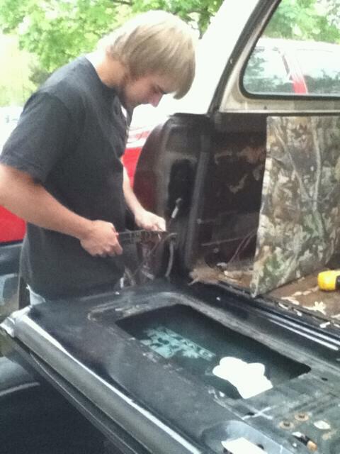 1979 Ford Bronco - A person is seen working on the rear tailgate area of a vehicle, with camouflage lining visible inside.