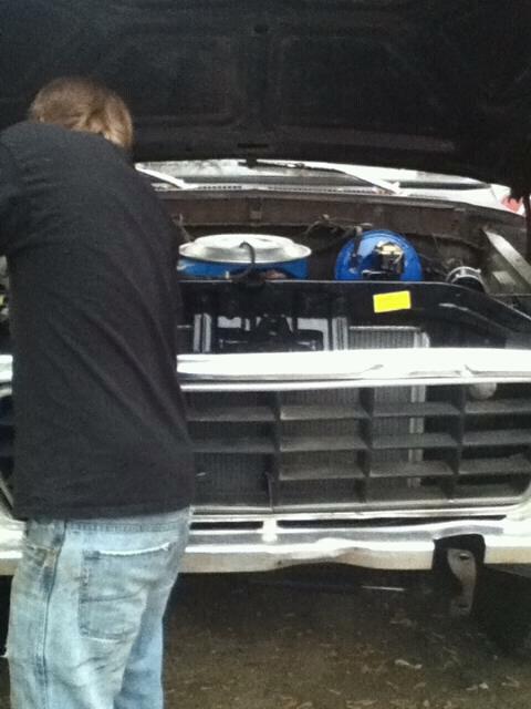 1979 Ford Bronco - Person working on the engine of a 1979 Ford Bronco, showing the front grille and engine components.