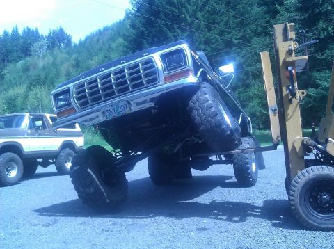 1979 Ford Bronco - A lifted black 1978 Ford Bronco is being repositioned by a forklift, with another Bronco visible in the background.